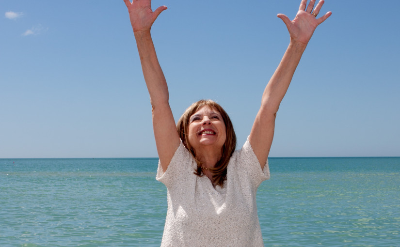Woman at beach raising arms to sky